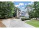 View of back exterior featuring a basketball hoop, oversized driveway, and mature trees at 6815 Fairgreen Dr, Suwanee, GA 30024