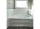 White bathtub with jets surrounded by white tile and a large, bright window at 5070 Smithfield Rd, Bowdon, GA 30108