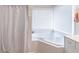 Corner bathtub with white tiled surround and shower curtain, offering a relaxing bathing experience at 115 Westbury Ln, Johns Creek, GA 30005