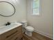 Neutral bathroom featuring wood-look floors, toilet, wood vanity with round mirror, and a view of the trees outside the window at 5567 Tyree Rd, Winston, GA 30187
