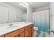 Well-lit bathroom includes double sinks, a vanity with wood cabinets, and a shower with a blue curtain at 823 Mackay Crk, Woodstock, GA 30188
