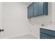 Well-lit laundry room featuring blue cabinetry with gold hardware, patterned floors, and a utility sink at 683 Summitt Hill Way, Cumming, GA 30040