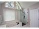 Bright bathroom featuring a glass enclosed shower and soaking tub, under a large A-frame window with tree views at 1052 Secret Ne Trl, Sugar Hill, GA 30518