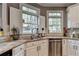 Well-lit kitchen featuring a stainless steel dishwasher, granite counters, and double windows with white shutters at 10355 Oxford Mill Cir, Johns Creek, GA 30022