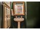 Elegant powder room features a pedestal sink, framed mirror, decorative artwork, and dark green walls at 2250 W Village Junction Se Way, Smyrna, GA 30080