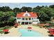 Stunning view of the white farmhouse with red roof, pool, red umbrellas, tables and chair sets, and lush landscaping at 679 Egrets Landing Lot 57, Covington, GA 30014