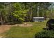 Wide backyard scene featuring a fire pit with stone border and large shed, surrounded by green trees and well-kept grass at 200 Sugar Mill Ln, Canton, GA 30115