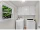 Functional laundry room with washer, dryer, built in cabinets, and a window looking out to the trees at 1953 Windcrest Sw Dr, Lilburn, GA 30047