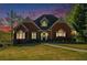 Inviting brick home with manicured lawn, landscaped garden beds, and warm interior lights visible through the windows at dusk at 2012 Golfers Way, Villa Rica, GA 30180