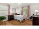 Bedroom with hardwood floors, two windows with pink curtains, and a comfy bed and dresser at 5641 Roberts Dr, Dunwoody, GA 30338