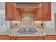 Close-up of stainless steel gas cooktop with wooden cabinets and granite countertops in kitchen at 866 Coopers Ridge Sw Path, Grayson, GA 30017