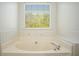 An oversized bathtub with tile surround beneath a window and green outdoor views at 560 Austin Dr, Mcdonough, GA 30252