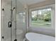Modern bathroom featuring a glass shower, soaking tub, and a large window with scenic backyard views at 5825 Rolling Oaks Dr, Cumming, GA 30040