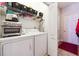 Compact laundry room with washer, dryer, storage shelves, and a white entry door at 5832 Sloane St, Douglasville, GA 30135