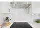 A cooktop beneath a stainless steel range hood is framed by white subway tile and white countertops at 3698 Annsbury Ct, Lilburn, GA 30047