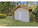 Close-up of a tan shed with a white door, surrounded by green grass and mature trees at 2520 Hartford Dr, Ellenwood, GA 30294