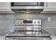 Close up of updated stainless steel stove and granite countertops with gray subway tile backsplash at 115 Braided Blanket Blf, Johns Creek, GA 30022