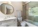 Bright bathroom featuring a vanity with white marble countertop, round mirror, and glass-enclosed shower and tub at 808 Lullwater Ne Rd, Atlanta, GA 30307