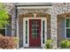 Close-up of a red front door framed by stone accents, flanked by green shrubs and a house number plaque at 4775 Columbia St, Cumming, GA 30040