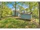 Backyard view of a blue house, mature trees, green grass, and a blue storage shed at 111 Amberwood Ln, Euharlee, GA 30145