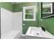 Renovated bathroom featuring subway tile in the tub, modern mirror, and green walls at 1217 Topaz Ln, Villa Rica, GA 30180