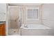 Bathroom featuring a tiled tub, glass shower, and white shuttered window at 8215 Majors Mill Dr, Cumming, GA 30041