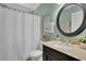 Well-lit bathroom with a round mirror, granite countertop, and tiled shower with a white curtain at 3870 Cabalzar St, Cumming, GA 30040