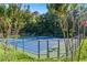 Community tennis court with blue and green surface surrounded by fence, trees, and flowering bushes at 6414 Blue Water Dr, Buford, GA 30518