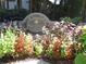 An ornate stone sign for Woodridge, A Condominium Community, is surrounded by colorful flowers and lush greenery at 4018 Woodridge Way, Tucker, GA 30084