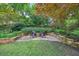 Cozy backyard patio with stone pavers, chairs, and a fire pit, surrounded by lush greenery and landscaping at 210 Malvern Pl, Roswell, GA 30076