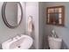 Stylish half-bath with a pedestal sink, round mirror, and wooden-framed window at 4236 Tacoma Trce, Suwanee, GA 30024