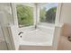 Close up of white soaking tub with tiled surround under bay windows with blind shade at 470 W Magnolia Cir, Johns Creek, GA 30005