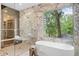This bathroom features marble walls, a glass shower, and a soaking tub with a view of the surrounding greenery at 0 Chattahoochee St, Roswell, GA 30075