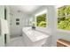 Bright bathroom featuring a soaking tub, glass shower, and a large window overlooking mature trees at 5040 Winding Branch Dr, Dunwoody, GA 30338