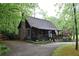A rustic log cabin featuring a stone chimney and inviting front porch, surrounded by lush trees and greenery at 6503 Old Macon Hwy, Rex, GA 30273