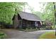 A rustic log cabin featuring a stone chimney and inviting front porch, surrounded by lush trees and greenery at 6503 Old Macon Hwy, Rex, GA 30273