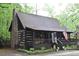 A rustic log cabin with a stone chimney and inviting front porch, set amidst a lush, green landscape at 6503 Old Macon Hwy, Rex, GA 30273