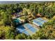 An aerial view of tennis courts and a pool with a large Clubhouse surrounded by a lush green forest at 4615 Kilmersdon Ln, Suwanee, GA 30024