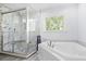 Modern bathroom featuring glass enclosed shower with marble tile and white soaking tub under window at 1488 Rivermist Sw Dr, Lilburn, GA 30047