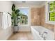 Bright bathroom featuring a large tub with travertine tile surround and a plant near a sunny window at 217 Knob Hills Cir, Decatur, GA 30030