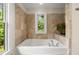 Bathroom featuring travertine tile surround, a drop in tub, and a window looking out to the trees at 217 Knob Hills Cir, Decatur, GA 30030