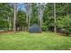 Grassy backyard with black garden shed nestled amongst tall trees and green foliage at 127 Stagecoach Trl, Stockbridge, GA 30281