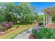 Landscaped front yard with mature trees, flowering plants, a brick path and a covered porch at 4592 Planters Hill Dr, Powder Springs, GA 30127