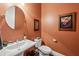 Stylish half-bathroom with a pedestal sink, round mirror, and warm terra cotta colored walls at 613 Brennan Dr, Decatur, GA 30033