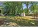 Large, grassy backyard featuring mature trees, play equipment, and a charming shed for storage at 5100 Sunset Maple Trl, Lilburn, GA 30047