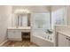 Bathroom boasts a luxurious tub with tile surround, a makeup vanity, and a large window with a view at 5100 Sunset Maple Trl, Lilburn, GA 30047