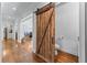 Hallway featuring a rustic barn door leading to a powder room, highlighting hardwood floors and open sightlines at 65 Maude White Rd, Kingston, GA 30145