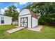 Exterior view of a backyard barn featuring white siding, wooden ramp entry, and gray trim details set on a stone base at 7307 Banks Mill Rd, Douglasville, GA 30135