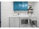 Well-lit laundry room with white washer and dryer, blue cabinets, and decorative tile flooring at 7390 Canter Run, Cumming, GA 30040