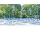 A large community pool with many lounge chairs, umbrellas, tables, and surrounded by a lush forest backdrop at 4507 N Peachtree Rd, Dunwoody, GA 30338